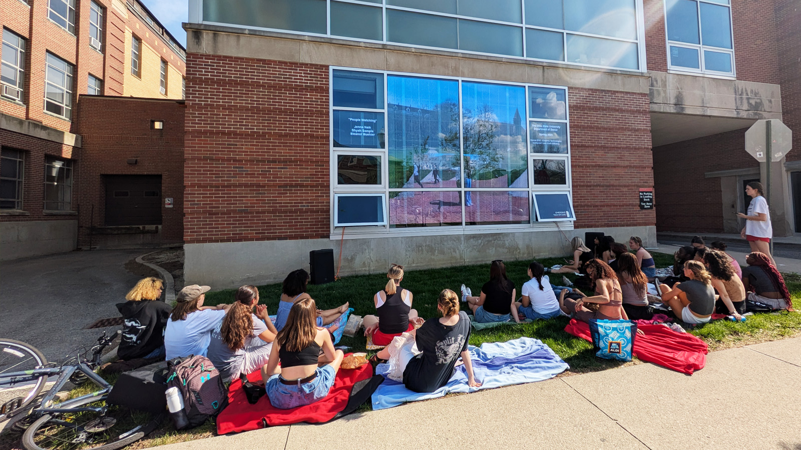 Students sitting on the outdoor lawn in front of the LED display
