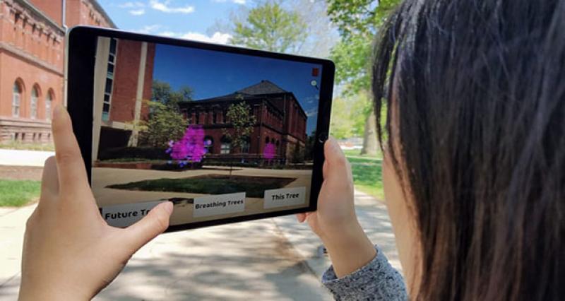 Student holding iPad outside with AR trees on screen