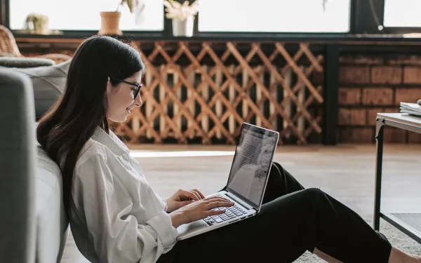 Woman leaning against couch using laptop