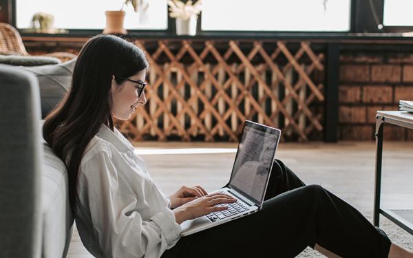 Woman leaning against couch using laptop