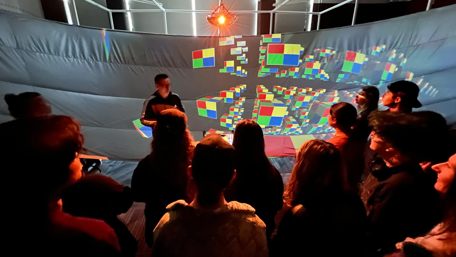 Students gathered around the immersive Hyve3D circular display, interacting with colorful virtual cube objects on the display